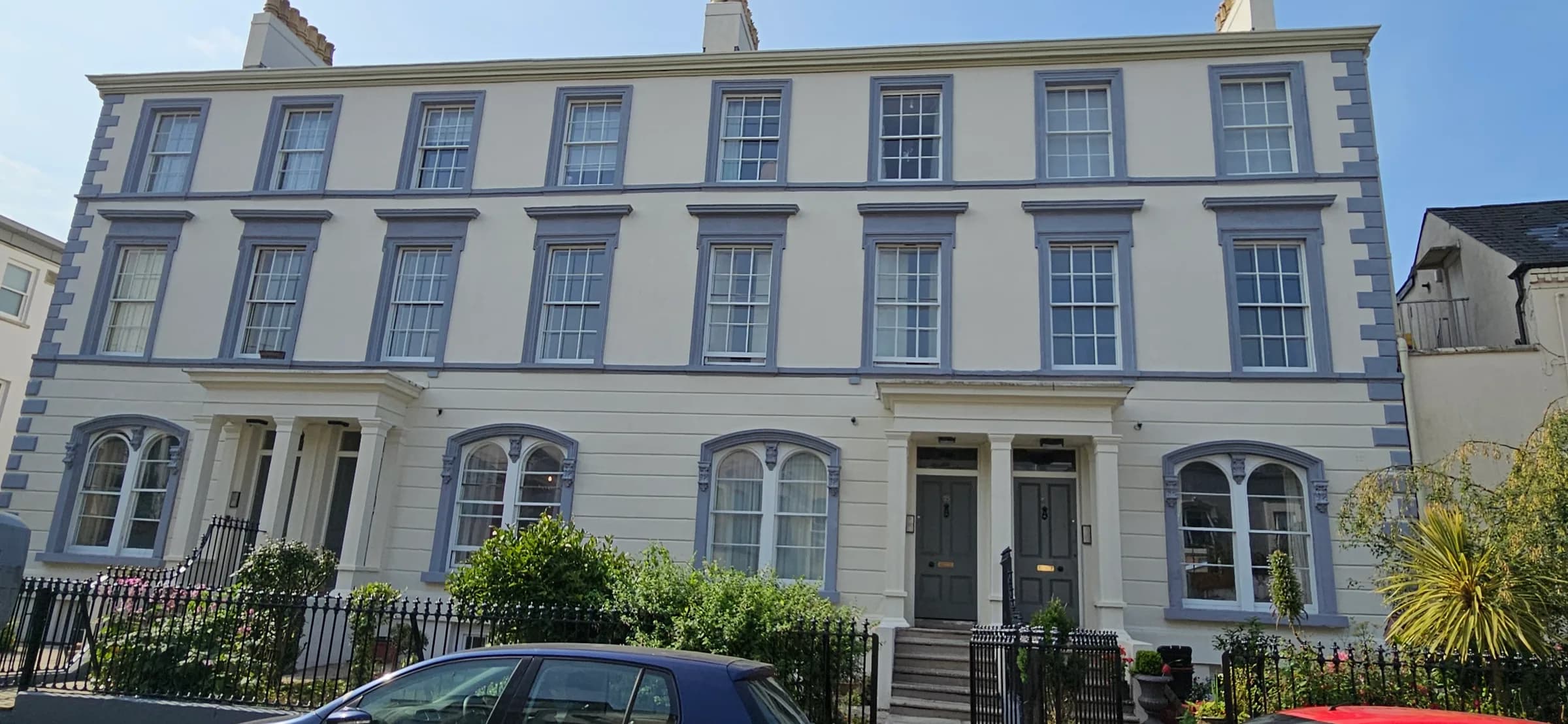 Cream-rendered Victorian terrace with blue-grey window surrounds and quoins, and grey front doors behind black railings