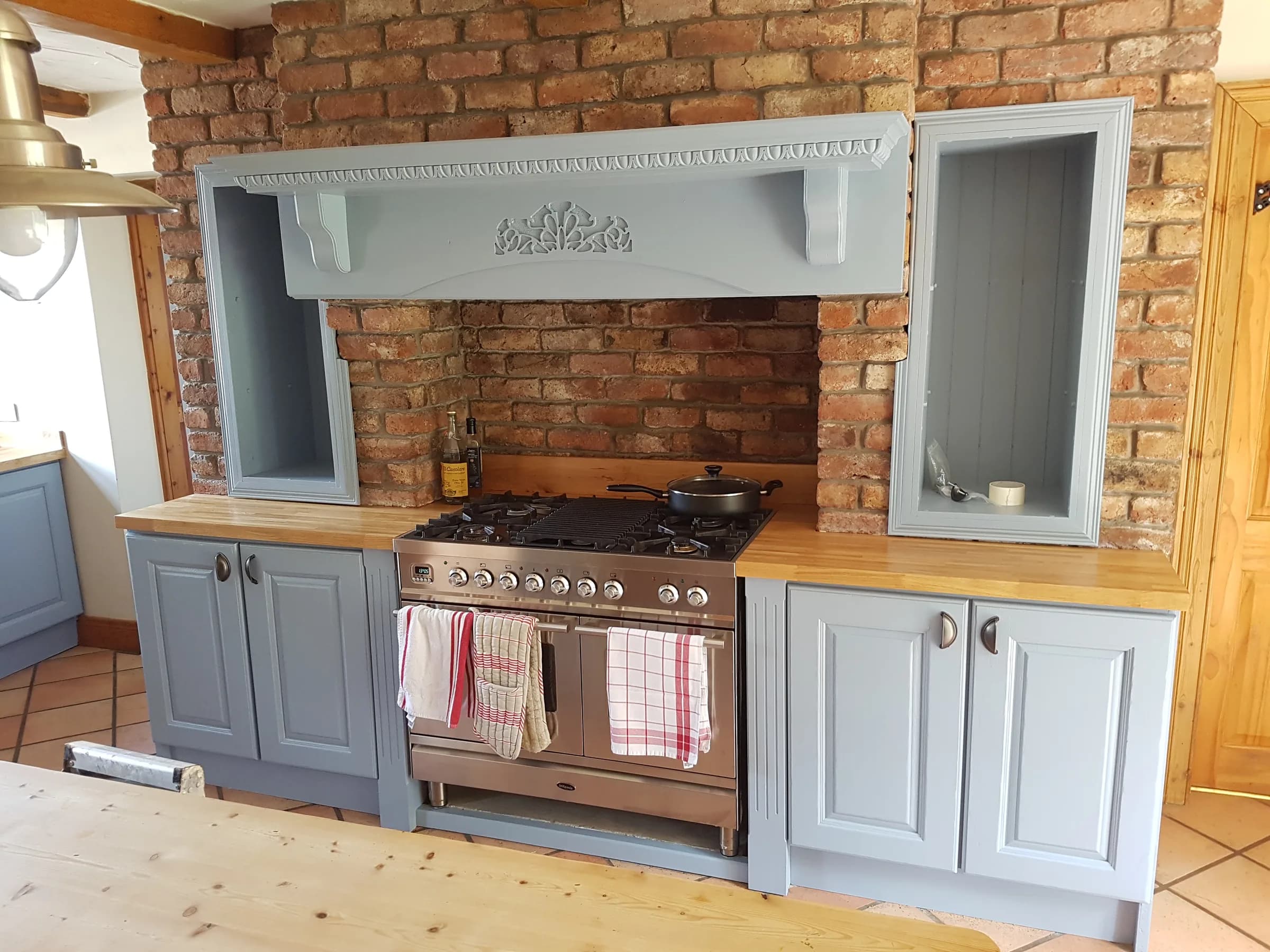 Farmhouse kitchen with an exposed red-brick chimney breast, a copper range cooker set into it, sage-painted cabinets and a solid wood worktop